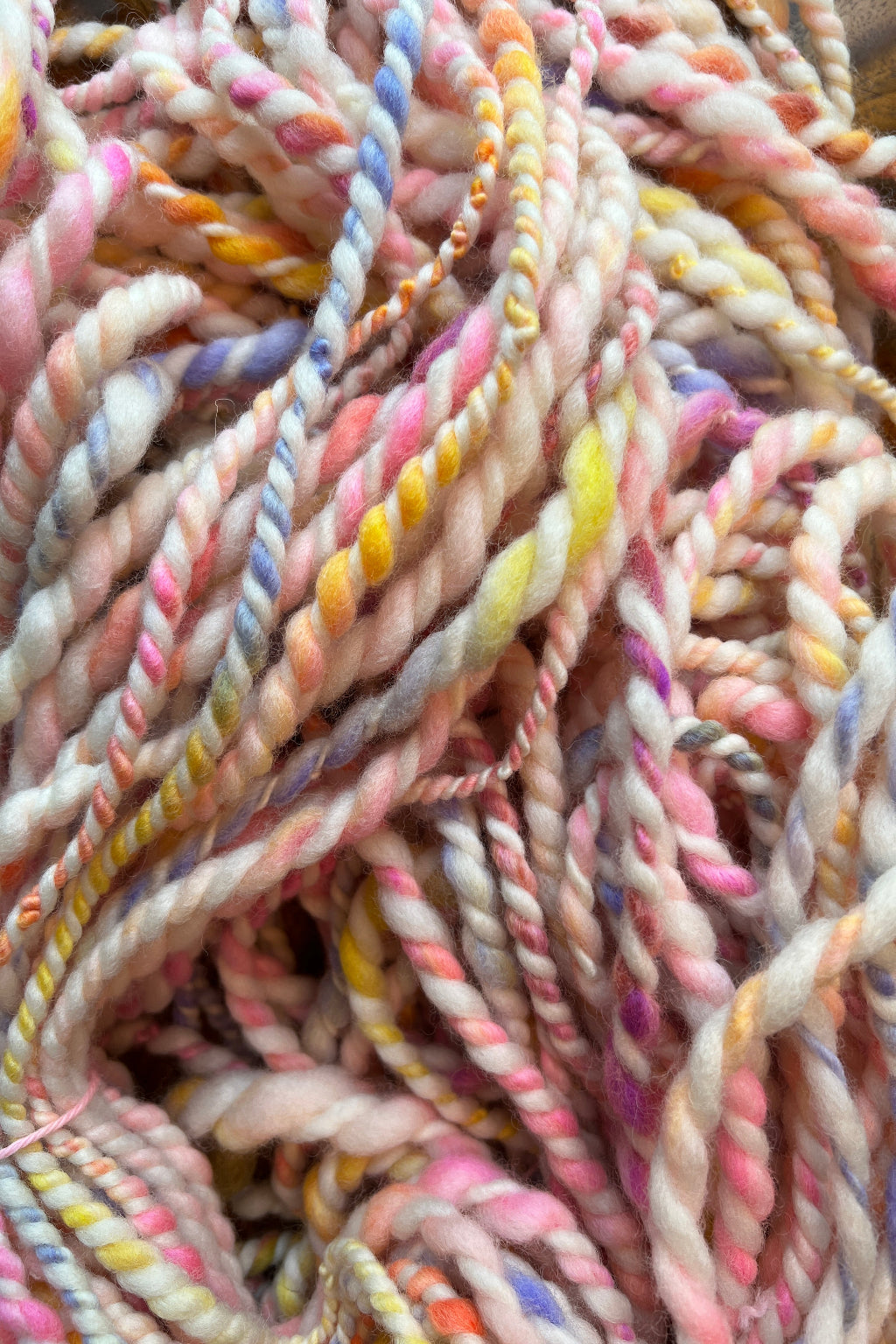 A close-up of twisted yarn or rope made from variegated cotton or wool fibers in soft pastel shades including pink, cream, yellow, blue, and purple. Hand-dyed and hand spun in Minneapolis.