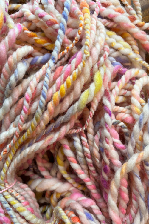 A close-up of twisted yarn or rope made from variegated cotton or wool fibers in soft pastel shades including pink, cream, yellow, blue, and purple. Hand-dyed and hand spun in Minneapolis.
