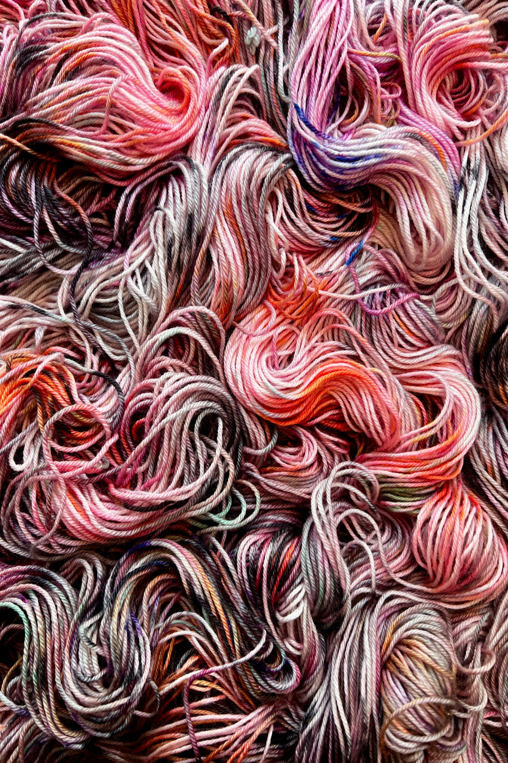 A close-up of Feral Little Jimothy colorway of variegated yarn in pink, coral, purple, gray, white, and orange tones. Hand dyed in Minneapolis by Painted Skein.