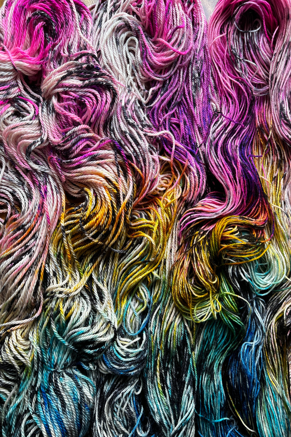 Close-up of variegated yarn skeins with swirling strands of pink, purple, beige yellow, green, blue, and black tones hand dyed in Minneapolis by Painted Skein in colorway Birch Rainbow.