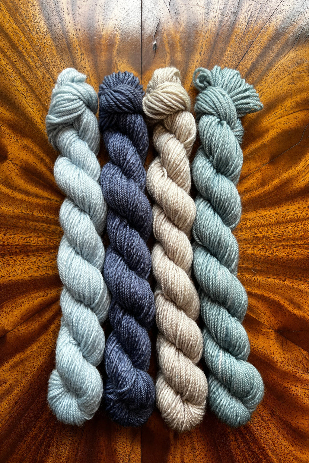 Four mini skeins of yarn in different colors; Frost Blue, Steel Blue, Drift Wood, Sea Glass.