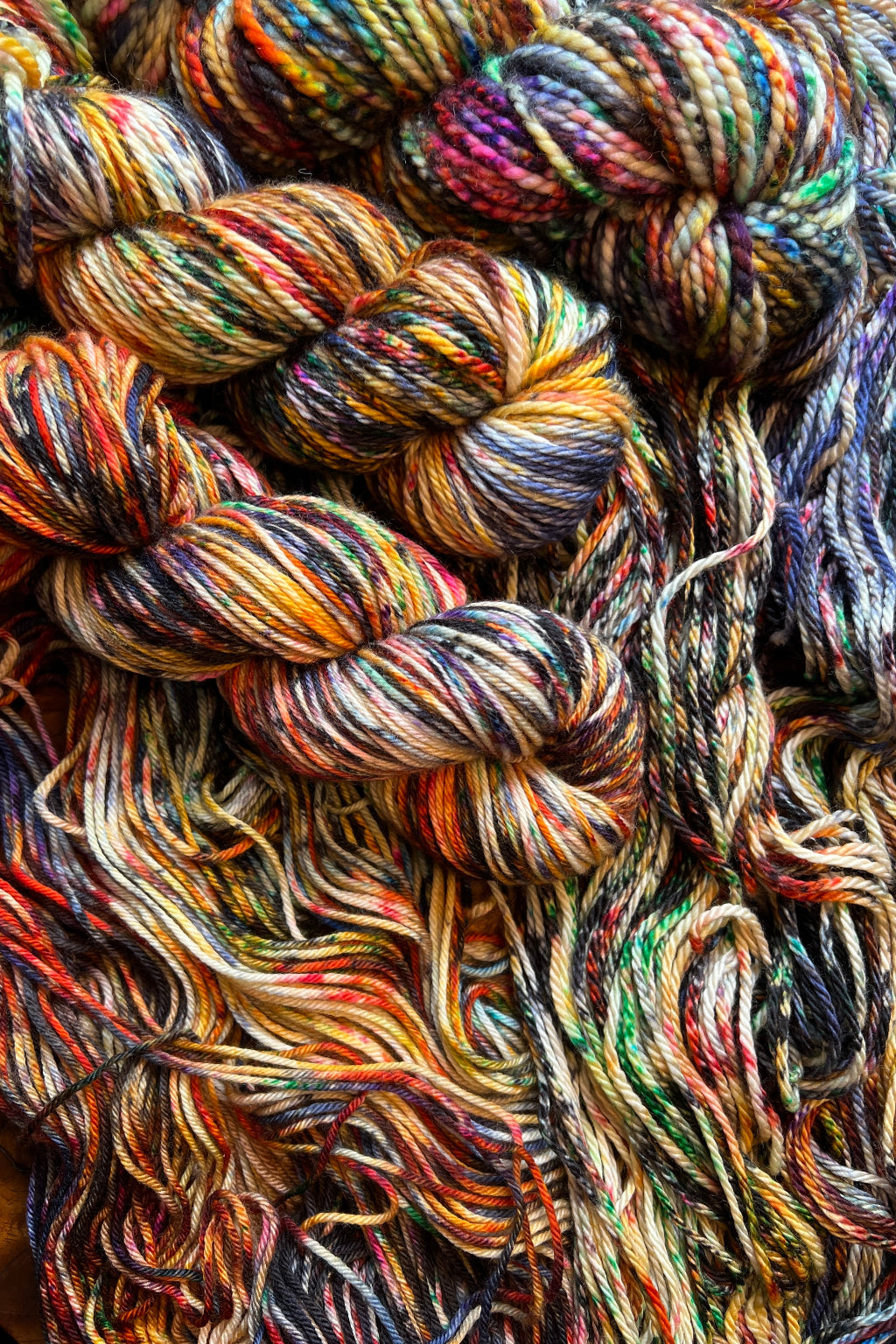 Lady with Fan hand-dyed yarn display with skeins of yarn. Hand dyed in Minneapolis by Painted Skein. Speckled merino wool yarn in tones of gold, red & pinks, blues, greens and black.