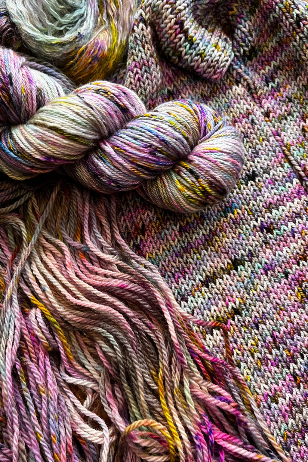 Summer Haze yarn display with skeins of yarn and knit sample. Hand dyed in Minneapolis by Painted Skein with magenta, pink, yellow, mint and brown tones.