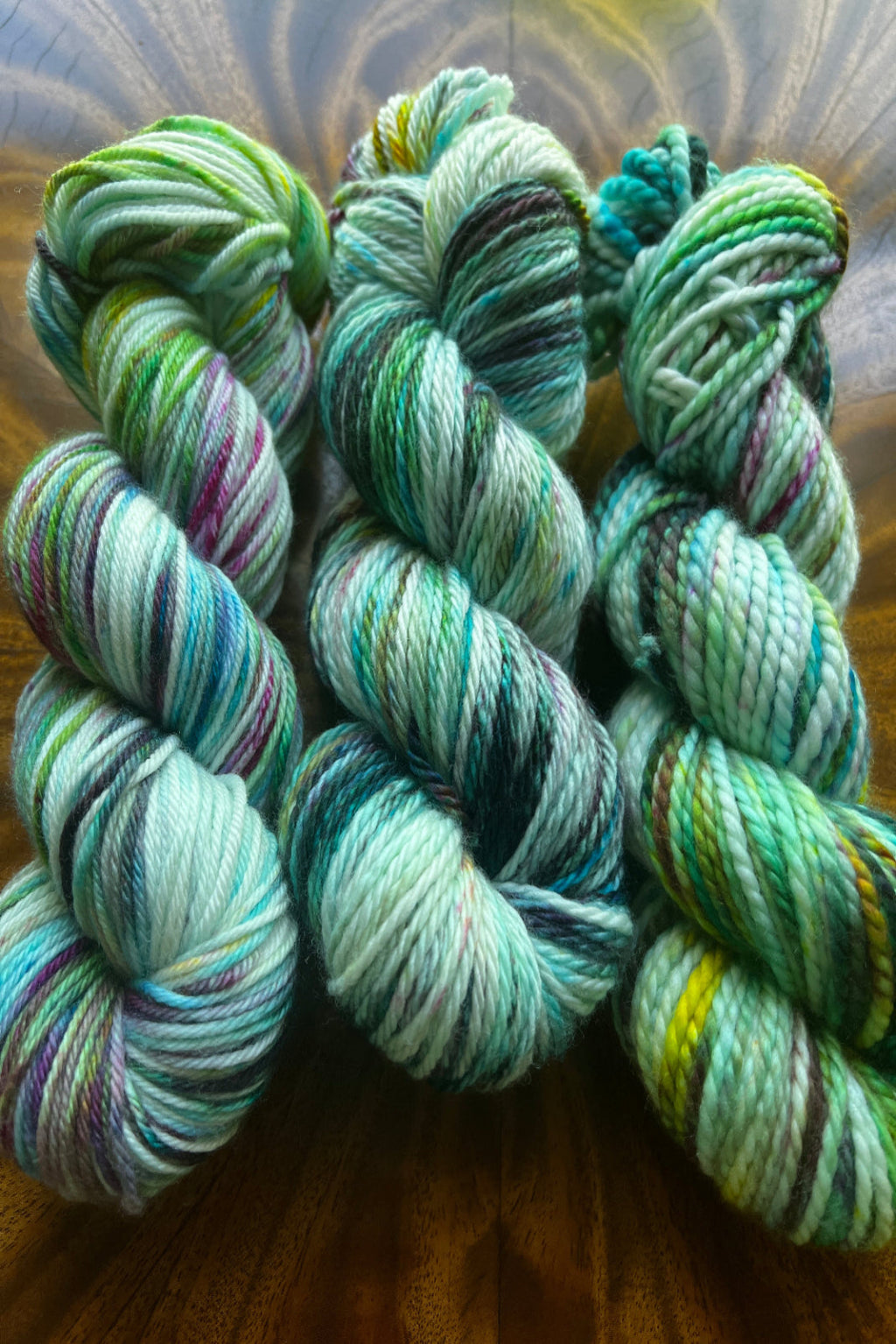 Three individual skeins of Neptune’s Garden yarn showing slight color variations in the small-batch blue, green, and black dye.
