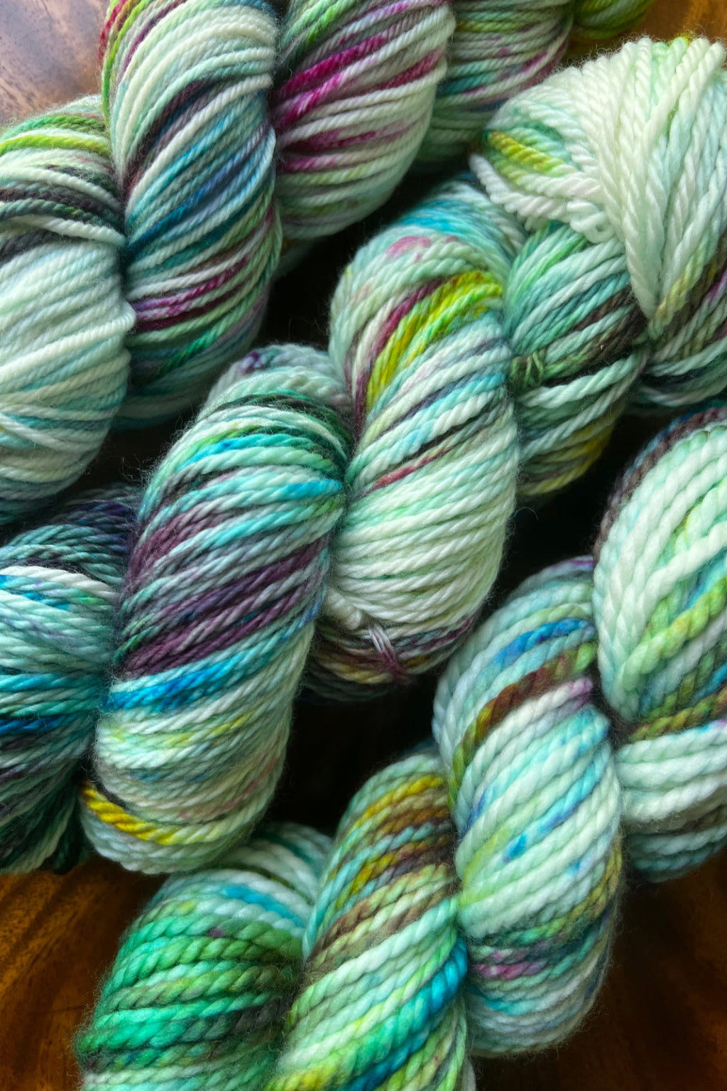 Twisted skein of Neptune’s Garden hand-dyed yarn in swirling shades of blue, green, and magenta with gold glints.