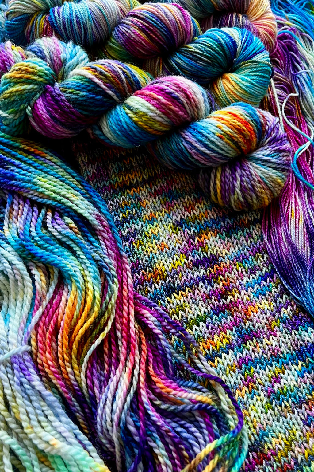 The Virgin hand-dyed yarn display with skeins of yarn and knit sample. Hand dyed in Minneapolis by Painted Skein with magenta, yellow, orange, purple, sapphire,  navy and greens.