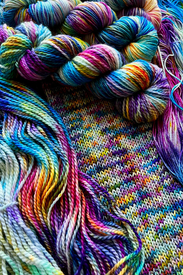 The Virgin hand-dyed yarn display with skeins of yarn and knit sample. Hand dyed in Minneapolis by Painted Skein with magenta, yellow, orange, purple, sapphire,  navy and greens.