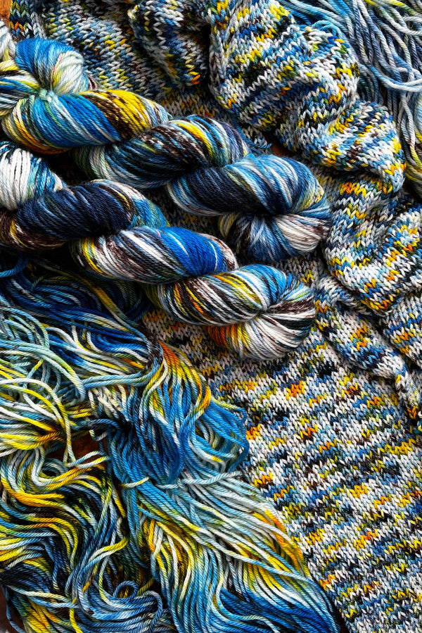 Painted Skein hand dyed yarn in the Starry Night colorway with swirling blues, golden yellow, and soft white inspired by Vincent van Gogh’s The Starry Night. Two twisted skeins, one flat skein and a scarf knitting sample. Hand-dyed in Minneapollis.