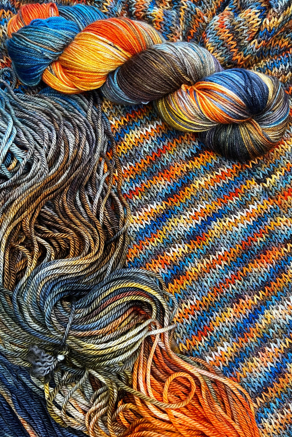 Painted Skein hand dyed yarn in The Scream colorway with swirling blues, golden yellow, bright orange, moody brown, sapphire and navy blue inspired by Munch's The Scream painting. One twisted skein, one flat skein and a scarf knitting sample. Hand-dyed in Minneapolis by Painted Skein.