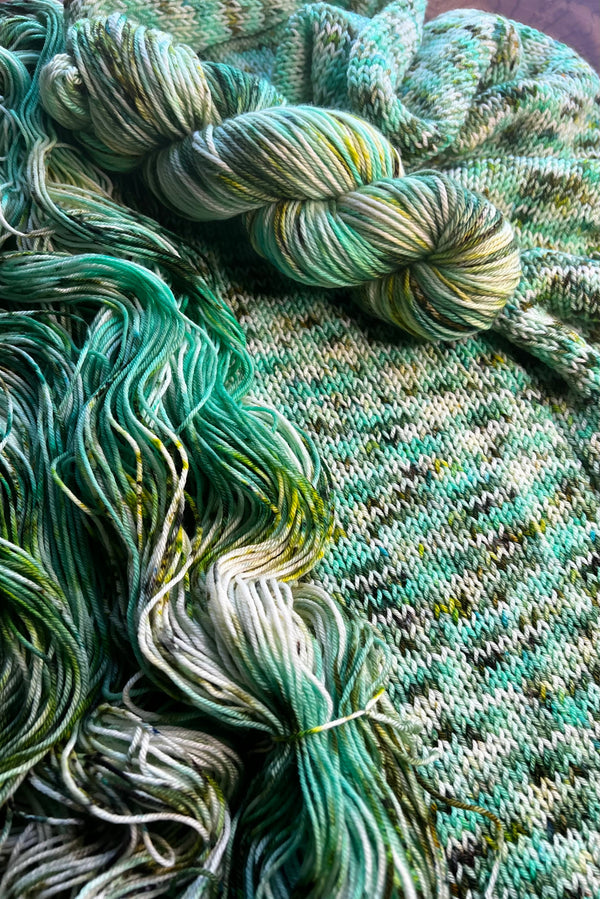 Van Gogh's Roses hand-dyed yarn display with skeins of yarn and knit sample. Hand dyed in Minneapolis by Painted Skein with forest, spearmint and spring green tones with speckles of moss green.