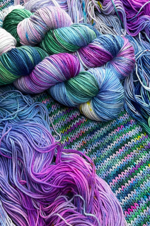 Water Lilies hand-dyed yarn display with skeins of yarn and knit sample. Hand dyed in Minneapolis by Painted Skein with hot pink, magenta, lavender and spring green, kelly green, baby blue tones.