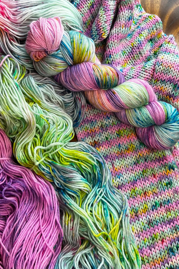 Primavesi hand-dyed yarn display with skeins of yarn and knit sample. Hand dyed in Minneapolis by Painted Skein with hot pink, peach, lavender and spring green,  tones with speckles of turquoise.