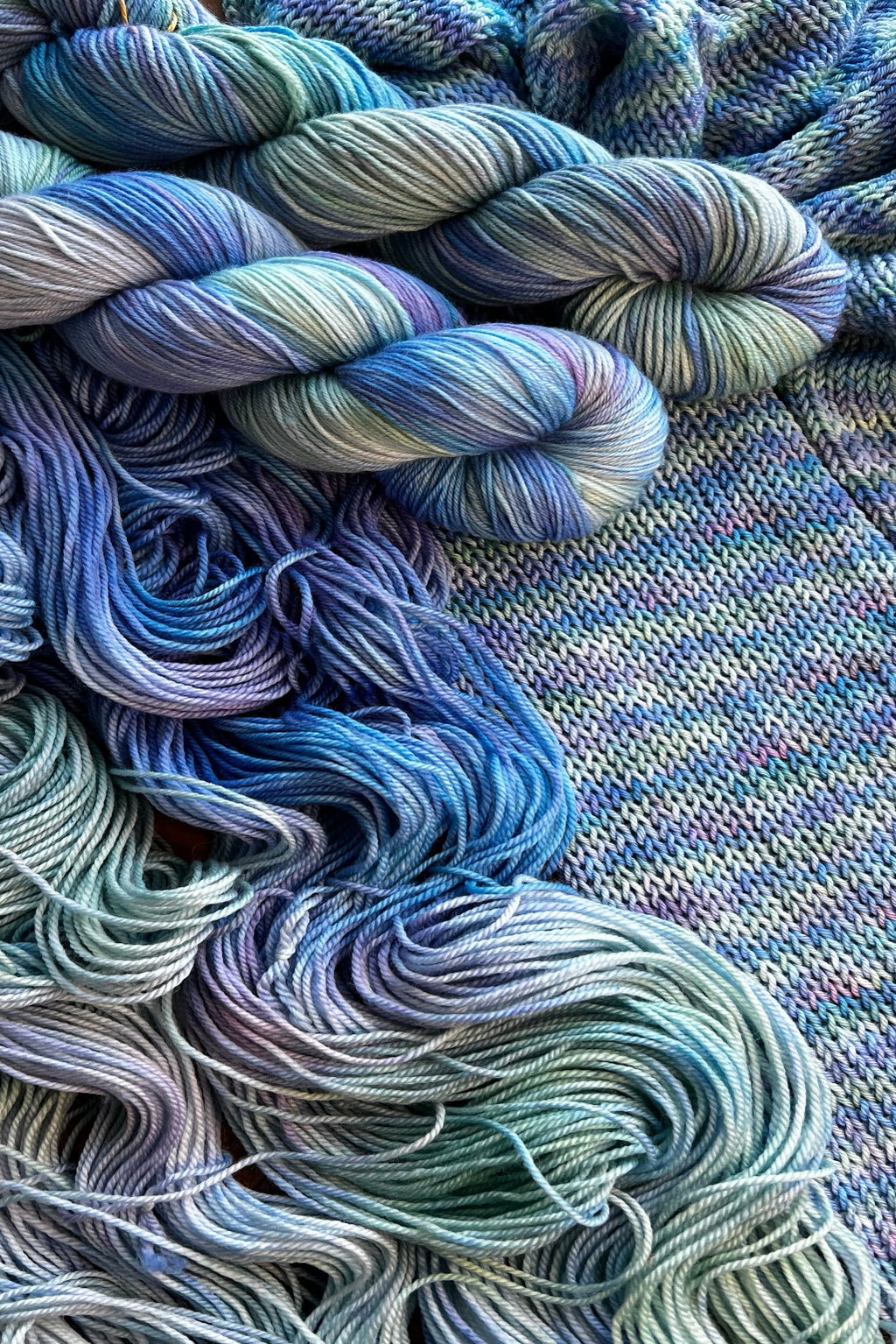 Painted Skein hand dyed yarn in the Reflections colorway with swirling blues, lavender and sage green inspired by Monet's Water Lilies  painting. Two twisted skein, one flat skein and a scarf knitting sample. Hand-dyed in Minneapolis by Painted Skein.