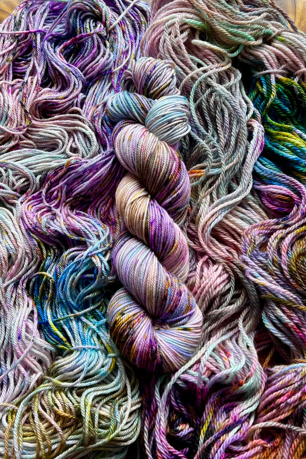 Summer Haze yarn display with skeins of yarn. Hand dyed in Minneapolis by Painted Skein with magenta, purple, blue, pink, yellow, mint and brown tones.
