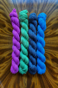 Four mini skeins of yarn in purple, green, blue, and dark blue hand dyed to coordinate with Monet Reflection colorway in Masterpiece Collection