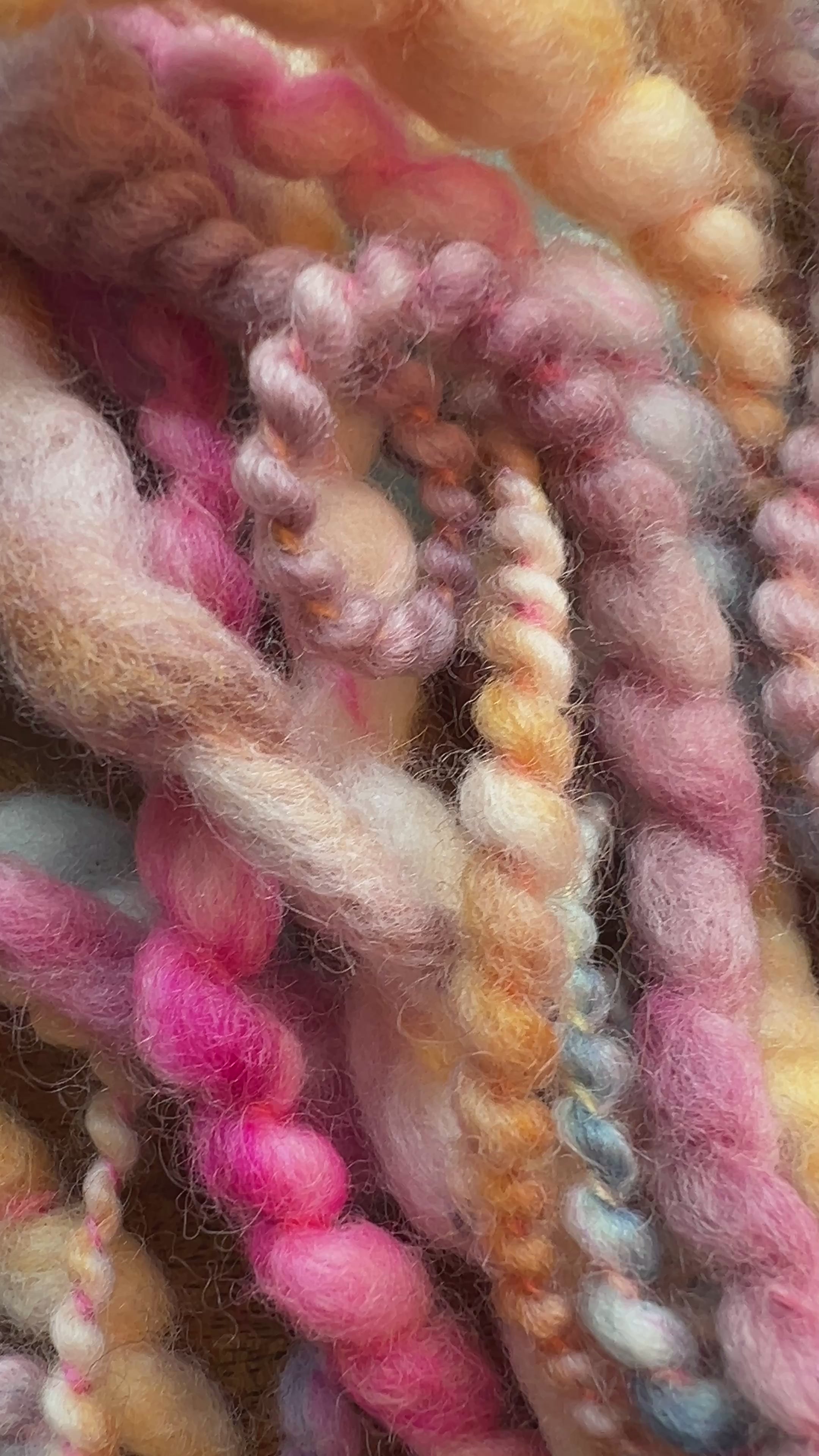 Video of  a close-up pile of chunky, twisted yarn in a variegated mix of pastel pink, mustard yellow, lavender, gray, and brown tones. Hand-dyed and hand spun in Minneapolis, merino wool.