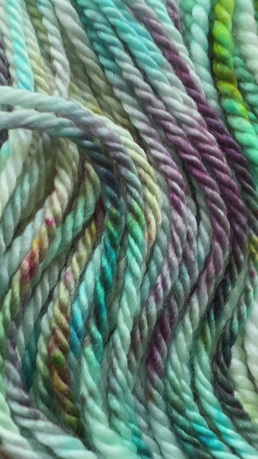 Close-up of Neptune's Garden yarn showing small-batch hand-dyed details in ocean blue, green, deep black, and coral magenta.