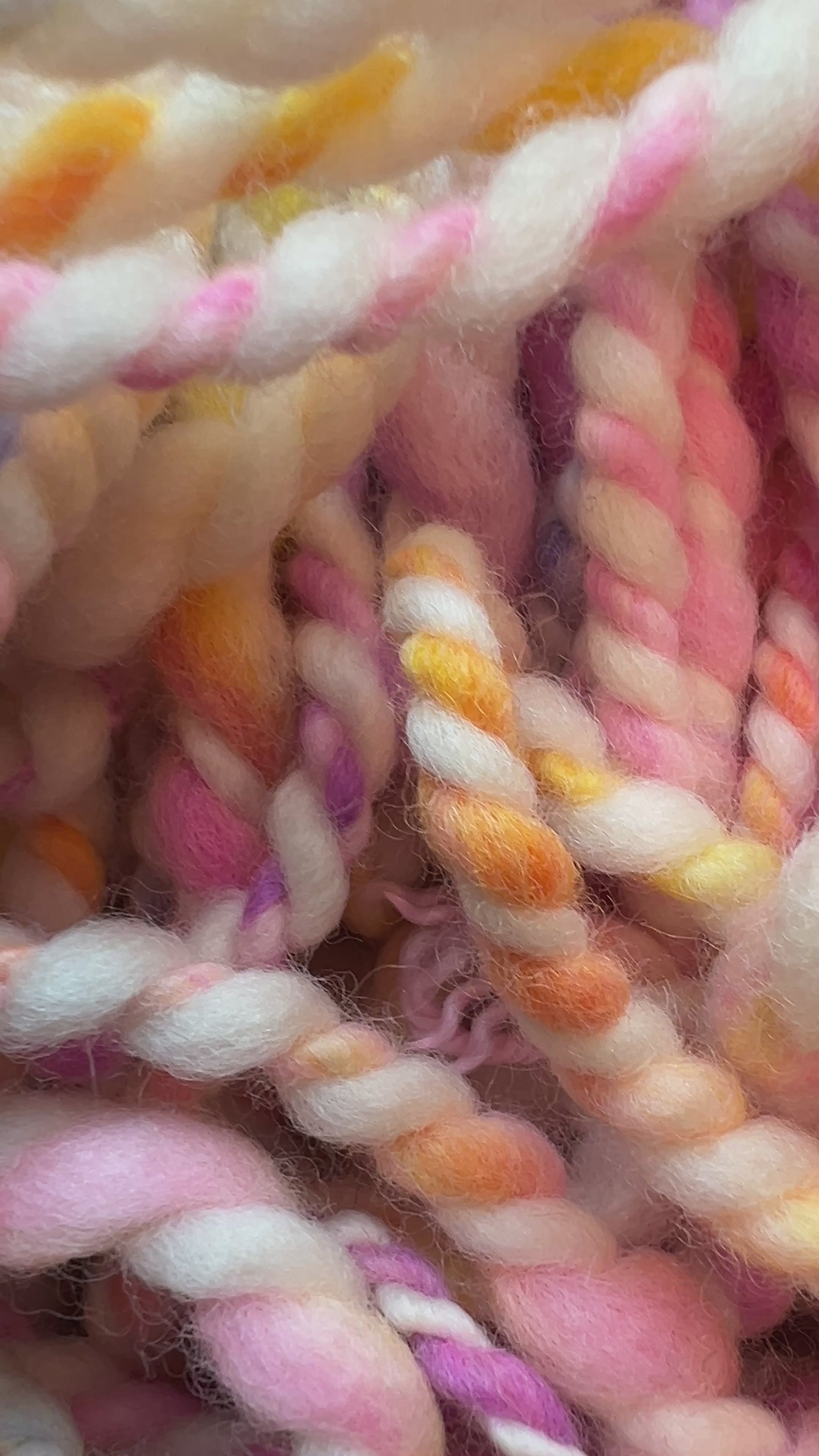 Video of a close-up of twisted yarn or rope made from variegated cotton or wool fibers in soft pastel shades including pink, cream, yellow, blue, and purple. Hand-dyed and hand spun in Minneapolis.