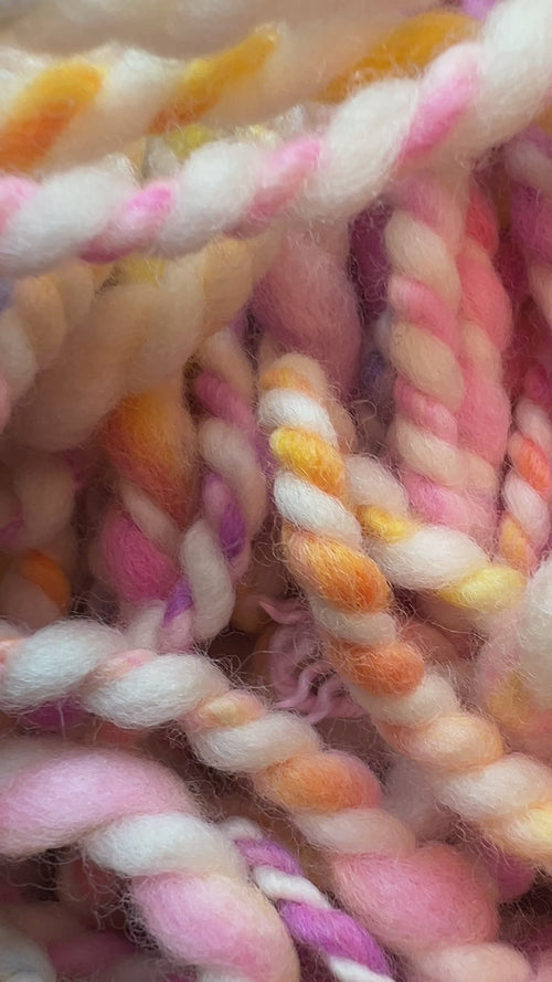 Video of a close-up of twisted yarn or rope made from variegated cotton or wool fibers in soft pastel shades including pink, cream, yellow, blue, and purple. Hand-dyed and hand spun in Minneapolis.